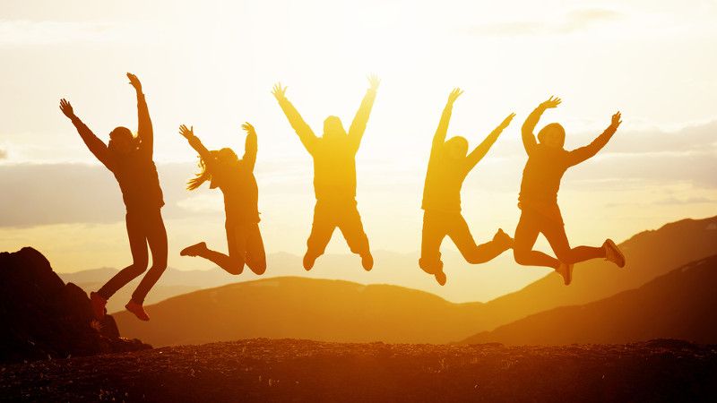 ludzie skaczą z radości w górach na tle zachodzącego słońca