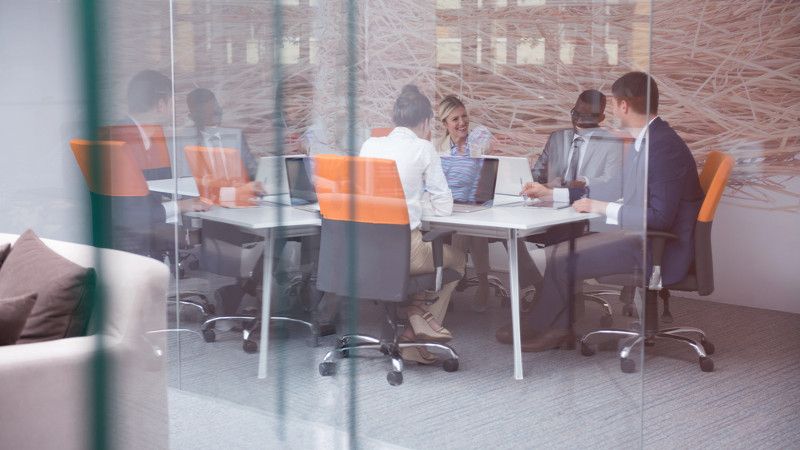 grupa elegancko ubranych ludzi siedzi przy stole z komputerami i się śmieje