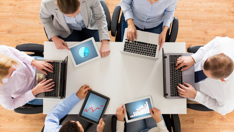 Ludzie siedzący przy jednym stole z laptopami