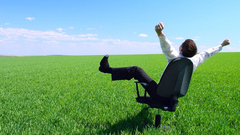 człwowiek w białej koszuli na biurowym krześle podnosi nogi i ręce do góry