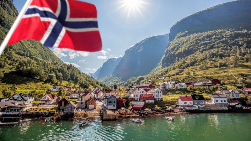 fiordy, dolina u-kształtna i flaga norwegii na tle przybrzeżnych drewnianych domków